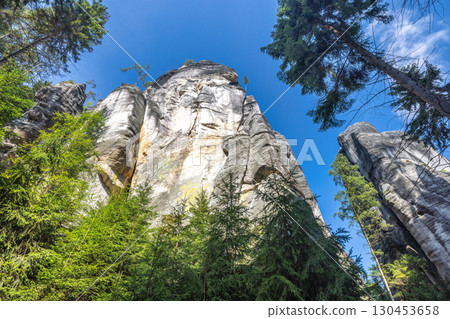 Adrspach-Teplice Rocks, sandstone formations in Hradec Kralove Region in Czech Republic, Europe. Unique rock formations rise against a clear sky, surrounded by lush green trees in a scenic landscape. 130453658