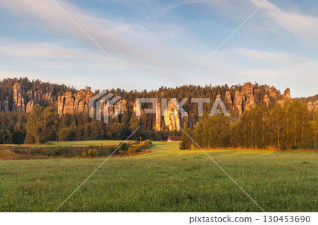 Adrspach-Teplice Rocks, sandstone formations in Hradec Kralove Region in Czech Republic, Europe. A scenic landscape featuring striking rock formations and lush green meadows, bathed in warm sunlight. 130453690