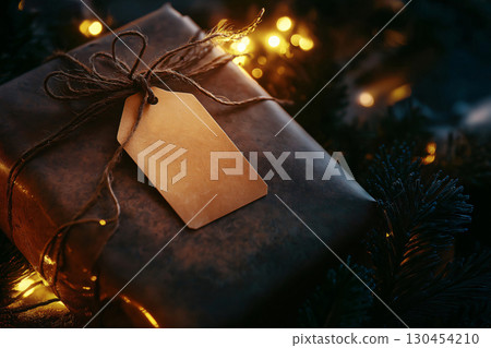 Christmas gift wrapped in brown paper and string with a blank tag on a blurry background with Christmas lights Christmas gift wrapped in brown paper and string with a blank tag on a blurry background with Christmas lights 130454210