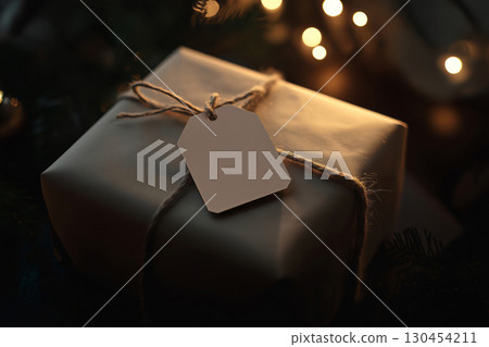 Christmas gift wrapped in brown paper and twine with a blank tag is laying under a Christmas tree with lights 130454211