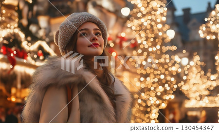Beautiful young woman wearing a fur coat and a wool hat is enjoying the magical atmosphere of Christmas lights at a traditional Christmas market 130454347