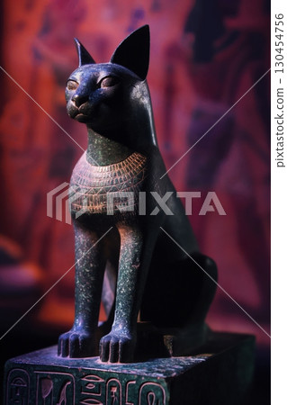 Dark green statue of Bastet, the Egyptian goddess of home and protection, sitting on a pedestal and illuminated with dramatic lighting 130454756