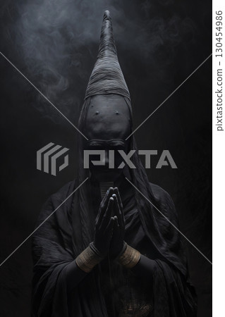 Mysterious dark priest wearing a long black robe and a tall headpiece is praying with his hands together 130454986
