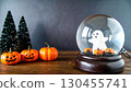 Cute ghost inside a glass snow globe surrounded by Halloween pumpkins and tiny trees. 130455741