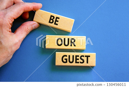 Be our guest symbol. Concept words Be our guest on beautiful wooden block. Businessman's hand. Beautiful blue background. Business and be our guest concept. Copy space. 130456011
