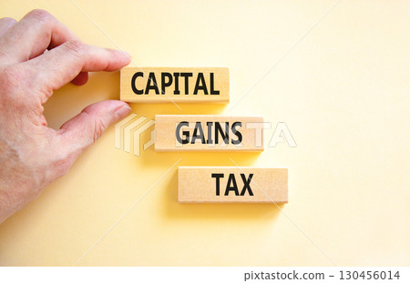 Capital gains tax symbol. Concept words Capital gains tax on beautiful wooden block. Businessman's hand. Beautiful white background. Business and capital gains tax concept. Copy space. 130456014