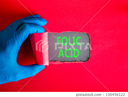 Folic acid symbol. Concept words Folic acid on beautiful grey paper. Doctor hand in blue medical glove. Beautiful red background. Medical healthy lifestyle folic acid concept. Folic acid symbol. Concept words Folic acid on beautiful grey paper. Doctor hand in blue medical glove. Beautiful red background. Medical healthy lifestyle folic acid concept. 130456122