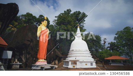 Tall Buddha Statue Beside White Stupa in Idyllic Setting Tall Buddha Statue Beside White Stupa in Idyllic Setting 130456586
