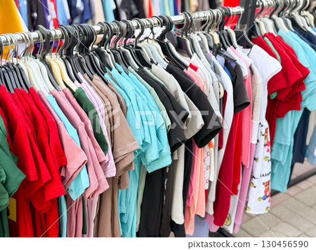 Close view of colorful t-shirts hanging in street retail market. Shopping, fashion, and lifestyle consumer concept in outdoor commerce. 130456590