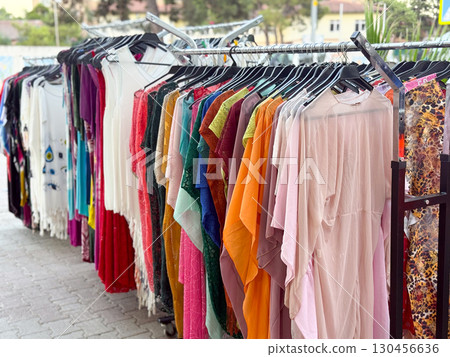Clothing rack with colorful dresses displayed in street market. Retail, shopping, and fashion concept in outdoor urban commerce environment. Clothing rack with colorful dresses displayed in street market. Retail, shopping, and fashion concept in outdoor urban commerce environment. 130456636