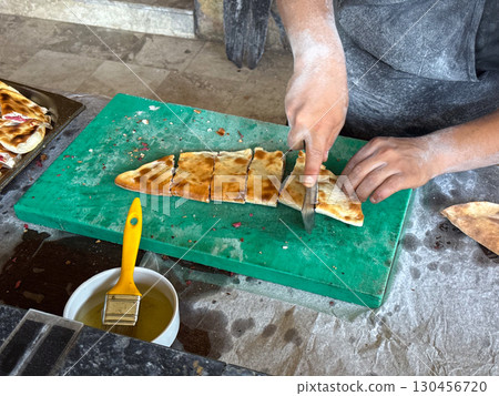 Chief Baked cuts flatbread on a table. Traditional cuisine, handmade preparation and authentic food culture. 130456720