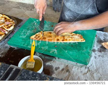Chief Baked cuts flatbread on a table. Traditional cuisine, handmade preparation and authentic food culture. 130456721