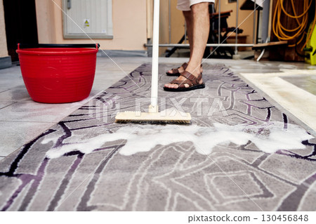 Man Cleaning a Rug with a Brush and Soapy Water 130456848