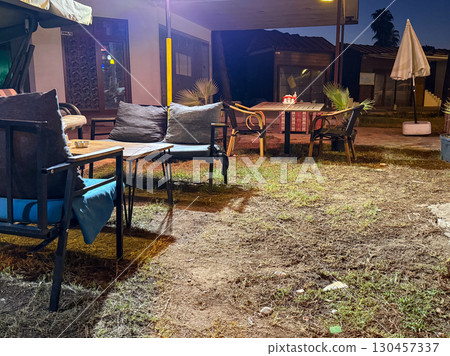 Outdoor cafe terrace with tables, chairs and sofas illuminated in the evening. Hospitality, leisure, service, social environment and comfort in a night setting. Outdoor cafe terrace with tables, chairs and sofas illuminated in the evening. Hospitality, leisure, service, social environment and comfort in a night setting. 130457337