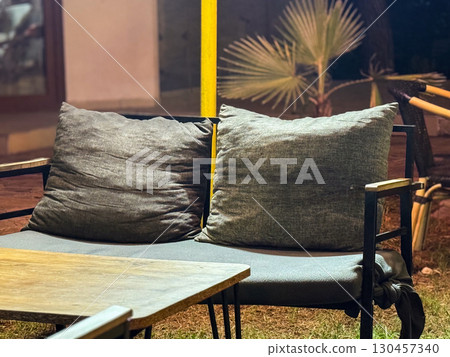 Outdoor sofa with large gray cushions placed near a table at night. Furniture, comfort, hospitality, leisure environment and relaxation space in a terrace. 130457340