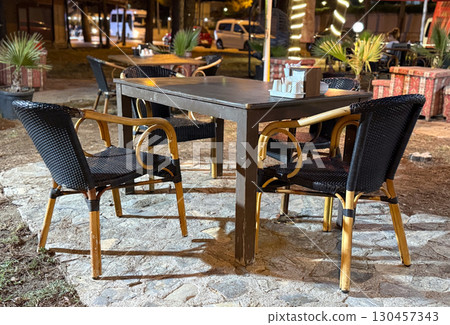Wooden table with chairs arranged outdoors in a night cafe. Hospitality, service, social dining, leisure atmosphere and evening restaurant environment. Wooden table with chairs arranged outdoors in a night cafe. Hospitality, service, social dining, leisure atmosphere and evening restaurant environment. 130457343
