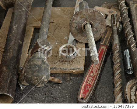 Set of Old Metal Tools on a Workbench A collection of old metal tools including wrenches, bolts, and rods placed on a dusty workbench. Set of Old Metal Tools on a Workbench A collection of old metal tools including wrenches, bolts, and rods placed on a dusty workbench. 130457359