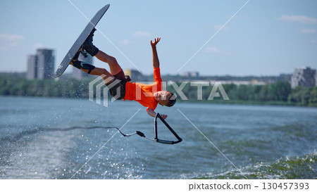 Young wakeboarder mid fall stunt with one hand release above water Young wakeboarder mid fall stunt with one hand release above water 130457393