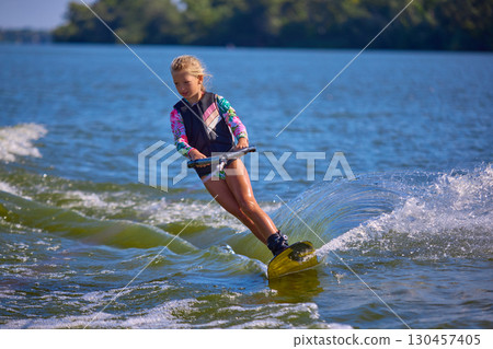 Young girl wakeboarding on lake with graceful lean and splash Young girl wakeboarding on lake with graceful lean and splash 130457405