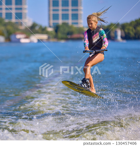Young girl wakeboarding and jumping high over lake wave 130457406