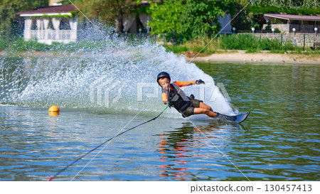 Boy water skier leaning sideways with spray trail of water 130457413