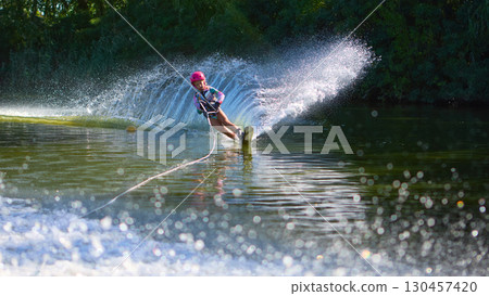 Young girl water skiing with pink helmet creating dramatic spray on lake Young girl water skiing with pink helmet creating dramatic spray on lake 130457420