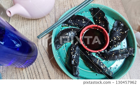 Black sesame dumplings arranged in a circle on a turquoise plate with dipping sauce 130457962