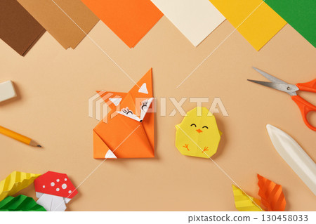 Paper fox and chick origami figures on desk with colored sheets, scissors, pencil, eraser and craft tools. Handmade creativity for kids. Paper fox and chick origami figures on desk with colored sheets, scissors, pencil, eraser and craft tools. Handmade creativity for kids. 130458033