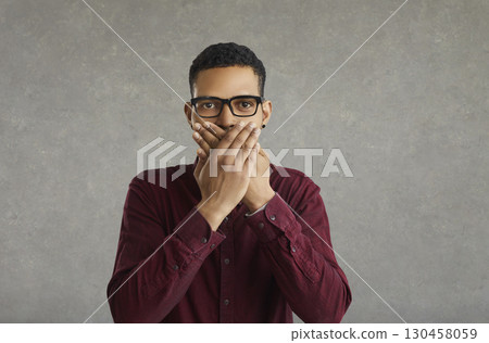 Portrait of an African American serious man who closes his mouth with both hands. 130458059