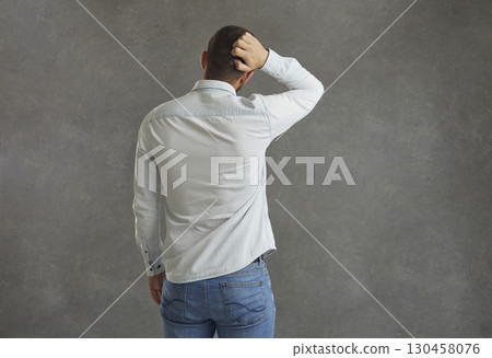 Unknown man stands with his back to the camera and scratches the back of his head in confusion. 130458076