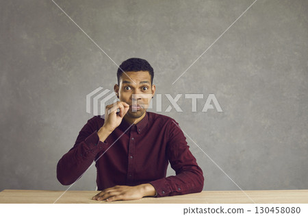 Black man sitting at desk and doing lip zip gesture promising to keep your secret 130458080