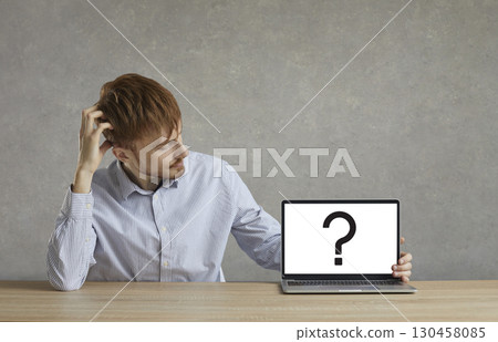 A man looks at a laptop screen with a question mark symbol. 130458085