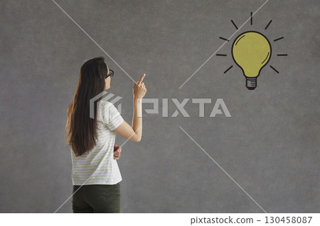 Smart college student having an idea and pointing at a light bulb on grey background Smart college student having an idea and pointing at a light bulb on grey background 130458087
