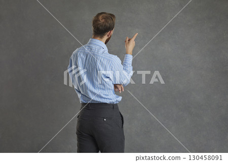 Focused businessman turned his back to the camera standing on a gray background. 130458091