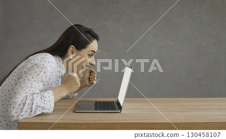Joyful emotional woman looking at laptop and shouting with happiness celebrating success. 130458107