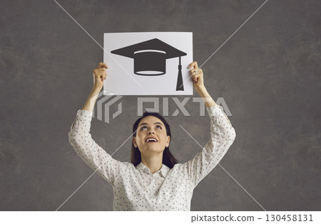 Happy student hoping to get university education holding image of square academic cap Happy student hoping to get university education holding image of square academic cap 130458131