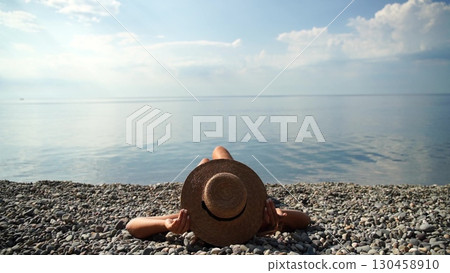 Beach hat summer: Hat lies on stony shore during summer for relaxation, reflecting calm sea water. Beach hat summer: Hat lies on stony shore during summer for relaxation, reflecting calm sea water. 130458910