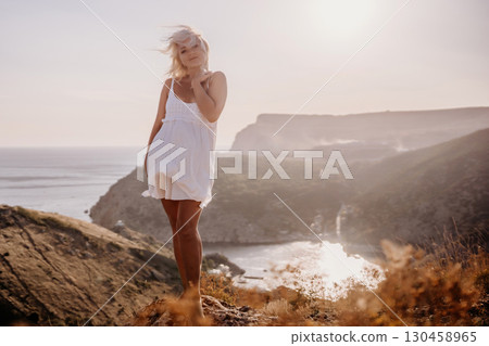 A blonde woman stands on a hill overlooking the ocean. She is wearing a white dress and she is enjoying the view. A blonde woman stands on a hill overlooking the ocean. She is wearing a white dress and she is enjoying the view. 130458965