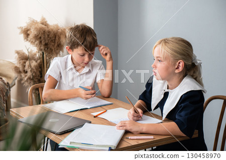 Children Studying Homework Classroom - Two children in school uniforms are seated at a table, working on their homework in a classroom. Children Studying Homework Classroom - Two children in school uniforms are seated at a table, working on their homework in a classroom. 130458970