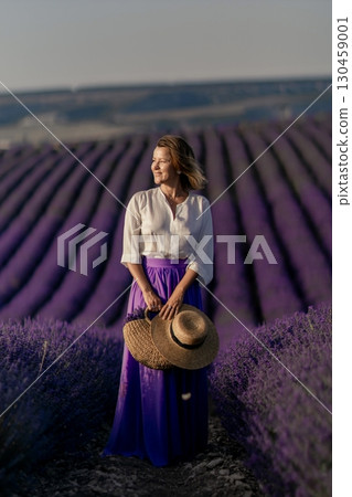 A woman wearing a purple skirt and a straw hat stands in a field of lavender 130459001