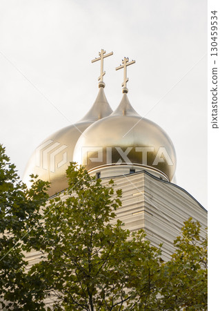 Golden domes of an Orthodox church with a cross, surrounded by trees. Modern Architecture Church Building in Paris. Golden domes of an Orthodox church with a cross, surrounded by trees. Modern Architecture Church Building in Paris. 130459534