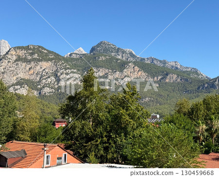 Mountain view with green forest and rocky peaks under the clear summer sky. Exploration, wilderness, ecology and serenity of natural landscape in outdoor adventure tourism. Mountain view with green forest and rocky peaks under the clear summer sky. Exploration, wilderness, ecology and serenity of natural landscape in outdoor adventure tourism. 130459668