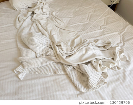 Closeup of white blanket and sheet with folds and creases on bed. Textile, comfort, domestic lifestyle, hospitality and accommodation environment detail. 130459706
