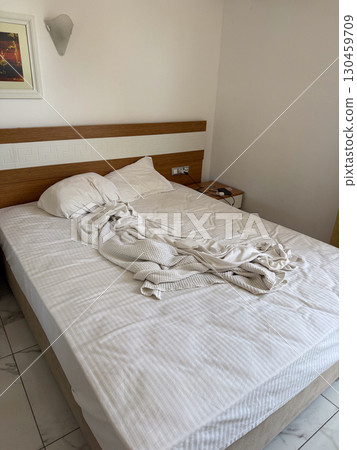 Unmade bed with pillow and blanket in a hotel room interior. Hospitality, travel, accommodation, rest, lifestyle and everyday domestic environment. 130459709