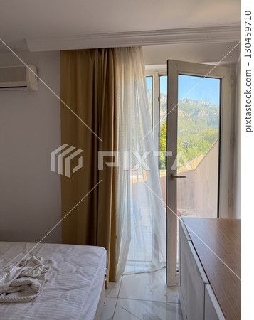 Hotel room with open balcony door and sunlight illuminating curtains and bed. Interior, accommodation, travel, relaxation and hospitality environment with morning atmosphere. 130459710