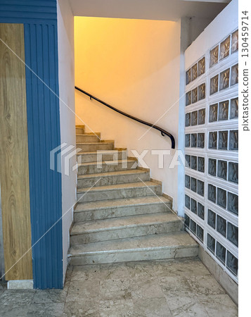 Marble staircase with handrail illuminated by yellow light inside a building. Architecture, construction, passage, interior design and functional indoor environment. Marble staircase with handrail illuminated by yellow light inside a building. Architecture, construction, passage, interior design and functional indoor environment. 130459714