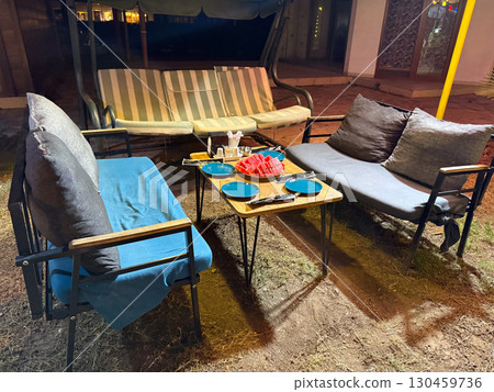 Outdoor table with plates, cutlery and sliced watermelon served in the evening. Hospitality, refreshment, leisure service, summer snack and social dining environment. 130459736