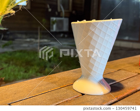 White ceramic cup with cone shape standing on a wooden table outdoors, copy space. Design, craft, utensil, object, hospitality environment and evening cafe atmosphere. White ceramic cup with cone shape standing on a wooden table outdoors, copy space. Design, craft, utensil, object, hospitality environment and evening cafe atmosphere. 130459741