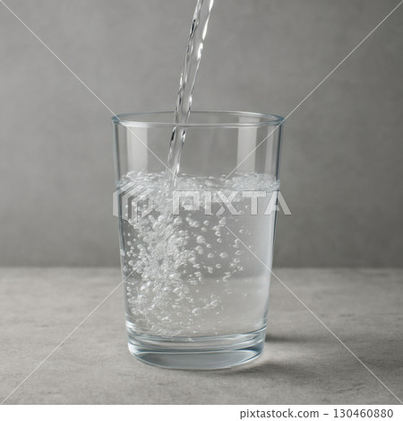Sparkling water being poured into clear glass, creating bubbles and refreshing look on stone surface with grey background Sparkling water being poured into clear glass, creating bubbles and refreshing look on stone surface with grey background 130460880