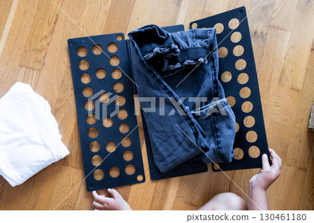 Child learning to fold clothes with a black folding board on wooden floor 130461180